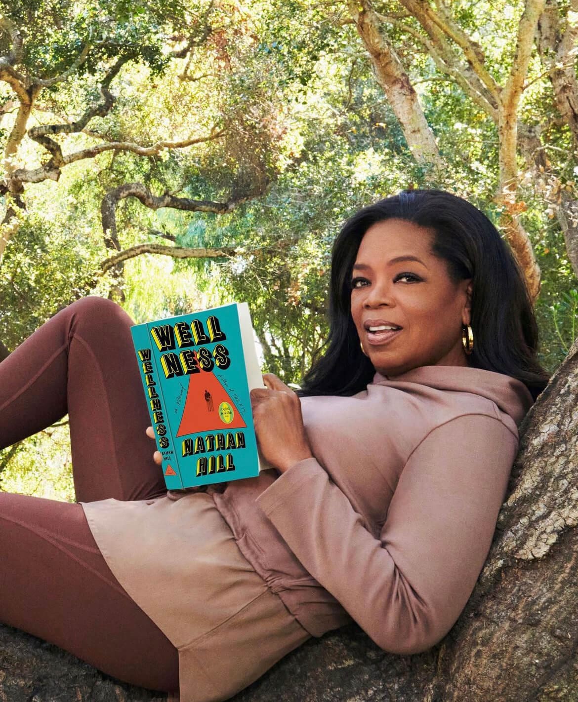 Oprah is sitting at a tree reading a book.