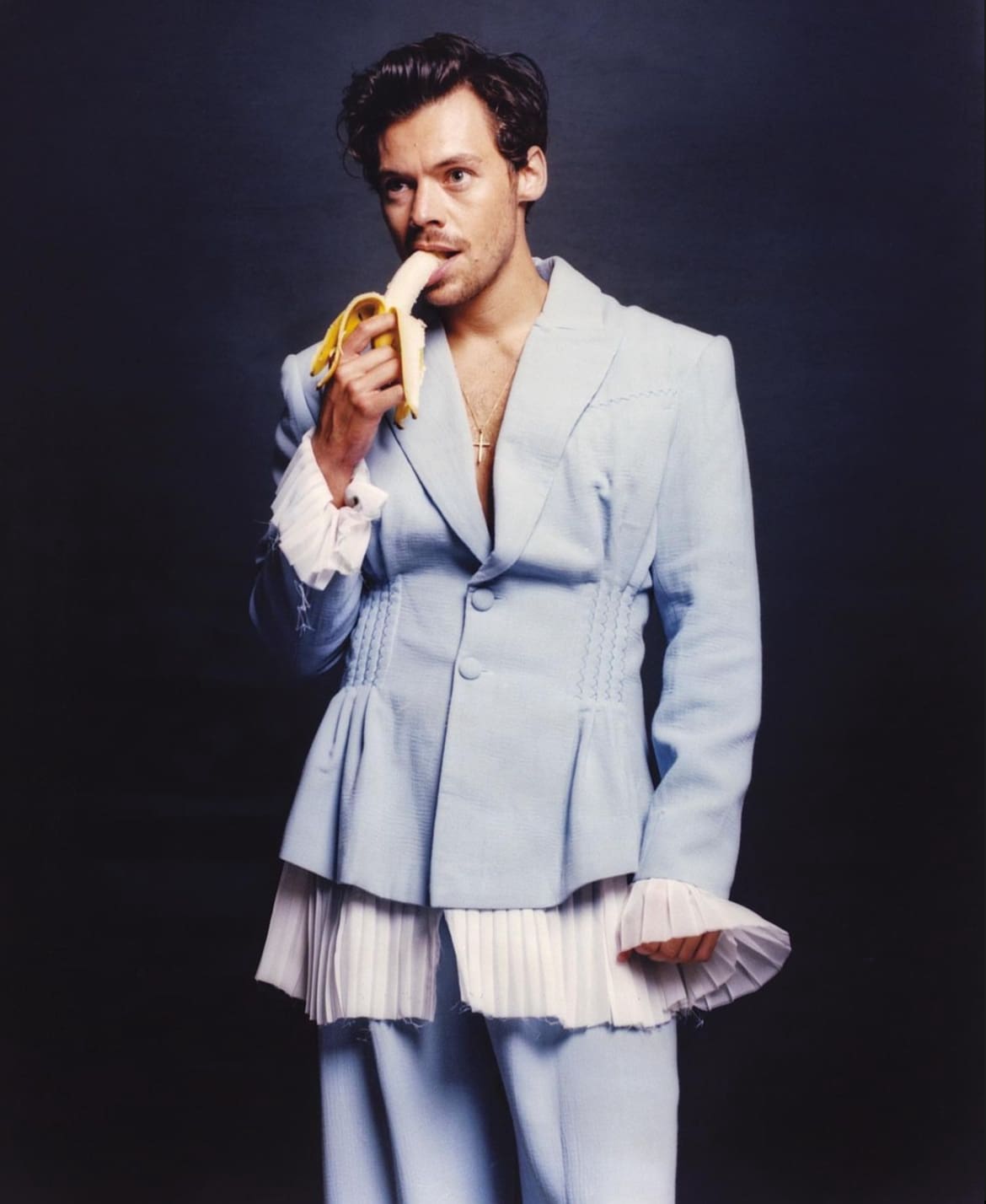 Harry Styles dressed nicely eating a banana. 